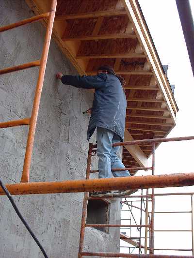 James picks out a few pieces of straw with pliers and fingers in order to prepare the outside wall for the second coat of plaster.