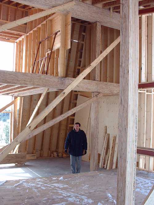 John Wilson stands in the living room. The second floor bedrooms are visible and open above. The sloped wall on the south is now enclosed.