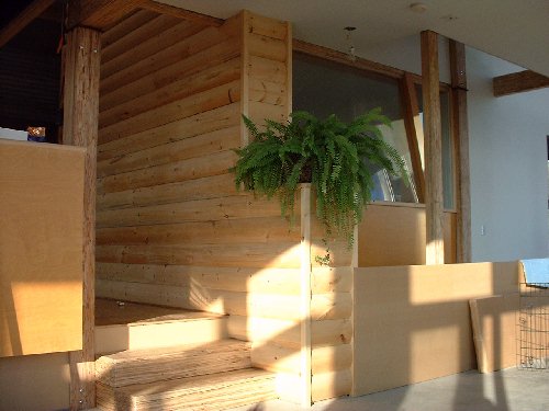 The new log cabin wall surrounds the master bedroom area. The glass sloped window on the right looks like a spaceship within the house looking out into the greenhouse on the south side from the master