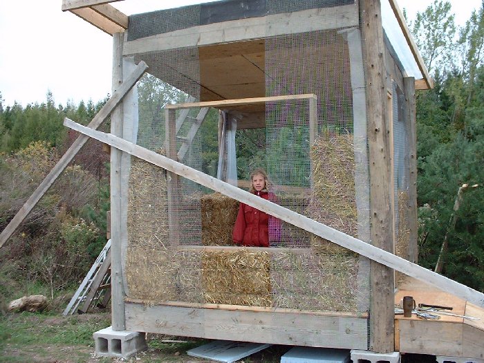 Claire peeks through the future window of her playhouse. Staw bale walls are half completed.