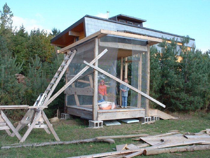 The kids and I create what I call a shed and they are calling a playhouse. The roof has already got the straw bales laid in the rafters. Claire and Ian help me prepare the chicken wire around the peri